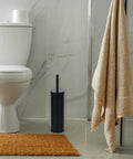 Heavy Duty Toilet Plunger With Sleek Floor Holder Kick Serious Bathroom Grime Monster Suction Unblocks Clogged Drains Real Quick Matte Black Sturdy Grip next to toilet.