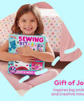 Smiling girl holding Kids Sewing Kit For Beginners: 6 Easy Projects Like Unicorn And Mermaid Pillows, sitting on bed.