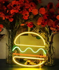 Multi-color LED burger neon sign amidst colorful flowers glowing in a dim room