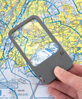 Hand holding Multi Power LED Lighted Pocket Magnifier With 2.5X Main Lens, 4.5X And 6X Lenses, over a map, showing magnification