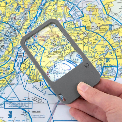 Hand holding Multi Power LED Lighted Pocket Magnifier With 2.5X Main Lens, 4.5X And 6X Lenses, over a map, showing magnification