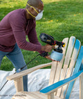 Person using iSpray Front End Nozzle for HVLP Sprayers for even coating on wooden chair outdoors.