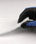Ceramic fiber insulation blanket, white, 1/4 in thick; close-up of its edge being peeled by a blue and black glove