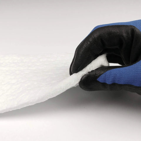 Ceramic fiber insulation blanket, white, 1/4 in thick; close-up of its edge being peeled by a blue and black glove