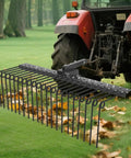 Tow Behind Lawn Dethatcher, 60 Inch Wide With 21 Steel Tines, Category 1 Three Point Hitch Tractor Attachment For Leaves, Pine Needles, Straw, And Grass, Fast Cleanups In Fewer Passes shown installed on a tractor in a field.