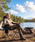 Person sitting by a lake on a Two Pack Lightweight Folding Camping Chairs For Adults With 4 Can Cooler Bag Cup Holder And Carry Bag