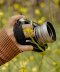 Photographer holding camera with Micro Clutch I Plate Hand Strap For Mirrorless Cameras With Low Profile Finger Loop in nature setting