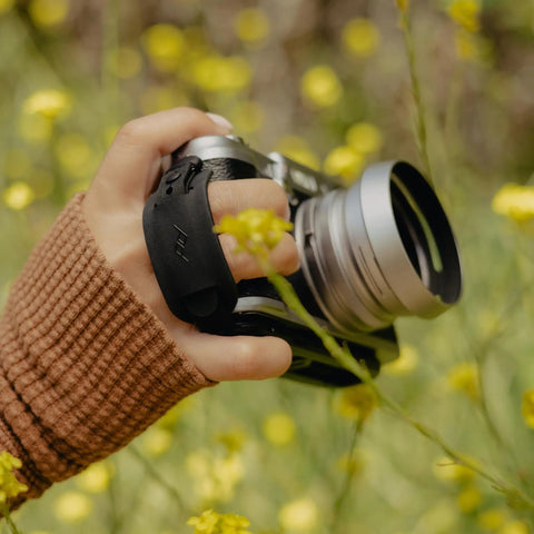 Photographer holding camera with Micro Clutch I Plate Hand Strap For Mirrorless Cameras With Low Profile Finger Loop in nature setting