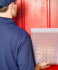 Rose Pink Holographic Padded Mailers 25x30cm Self Seal held by person in blue in front of a red door