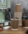 80 Pack 10 Oz Insulated Paper Coffee Cups With Lids And Straws Ripple Wall Three Layer Brown Hot Beverage Cups next to coffee machine