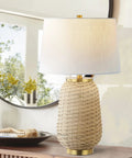Brass Gold And Light Brown Rattan LED Table Lamp With White Linen Shade, 25 Inches Tall, on a wooden console near a mirror.