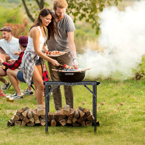 Foldable Grill Table With 3 Height Settings Up To 29.5 Inches Lightweight Camping Table With Heat Resistant Mesh Top Waterproof Portable Handle For Outdoor Cooking BBQ Tailgate Or Picnic Setup in use outdoors with people grilling