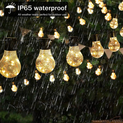 Battery Operated 25 Feet 100 LED Warm White Hanging String Lights With 20 Bulbs Remote Dimmable Eight Modes Memory Timer Waterproof And Shatterproof For Indoor Outdoor Decor Perfect For Bedroom Patio Balcony Home And Christmas Party shown glowing in rain