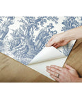 Applying Country Life Toile Peel And Stick Wallpaper Roll For Easy DIY Accent Wall Blue And White No Water Needed Quick Peel And Stick Application 20.5 Inches Wide By 16.5 Feet Long 100 Percent Removable No Sticky Residue Renters Friendly to wooden surface.