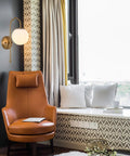 Gold Wall Sconce LED Globe Frosted Glass Shade Modern Bedside Light Fixture for living room with brown chair and window nook.