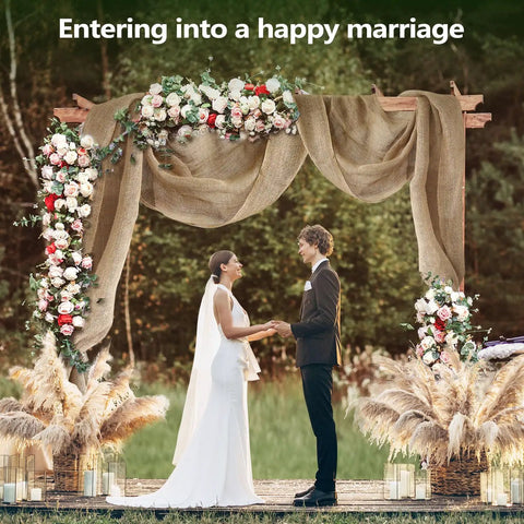 Wedding arch decorated with natural burlap fabric, flowers, and pampas grass outdoors with couple under arch.
