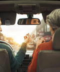 Two people in car interior, rear view, driver and passenger interacting, focus on hands, car dashboard visible.
