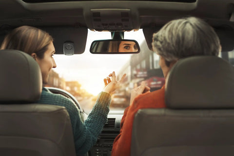 Two people in car interior, rear view, driver and passenger interacting, focus on hands, car dashboard visible.