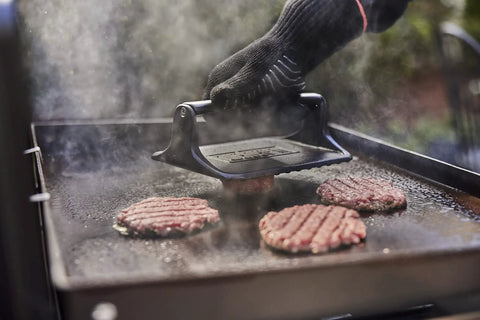 Heavy Duty Weber Griddle Press For Perfect Bacon, Smash Burgers And Crispy Paninis pressing burger patties on a hot griddle.