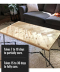 Wooden coffee table with natural finish in living room, couch and decor visible. Text about curing time for table surface.
