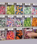 A wall-mounted candy display with various colorful bins containing candies like mint, gum, and butter creams in labeled sections.