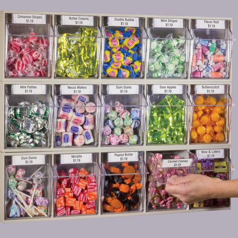 A wall-mounted candy display with various colorful bins containing candies like mint, gum, and butter creams in labeled sections.