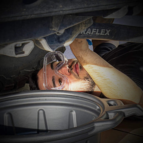 Clear Protective Lab Safety Goggles ANSI 287.1 Approved worn by man working under vehicle with ventilation and comfy fit design.