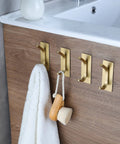 Brushed Gold Self Adhesive Wall Hooks Four Pack Stainless Steel Towel Coat Hat Robe Hangers For Bathroom And Kitchen No Drill Easy Install Rustproof Strong Hold In Wet Environments on wooden surface