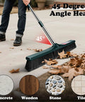 Heavy Duty Outdoor Push Broom With Hella Durable Stiff Bristles And 58 Inch Long Handle sweeping leaves at 45 degrees on concrete.