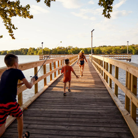 Children playing on a dock, one holding a Kids Fishing Rod And Reel Combo, 29 Inch Floatable Spincast Set With 20 Size Reel.