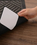 Hand applying Rug Gripper Set Of 4 Non Slip Corner Pads For Hardwood Floors And Tile on a rug edge, showing adhesive side on wood floor.