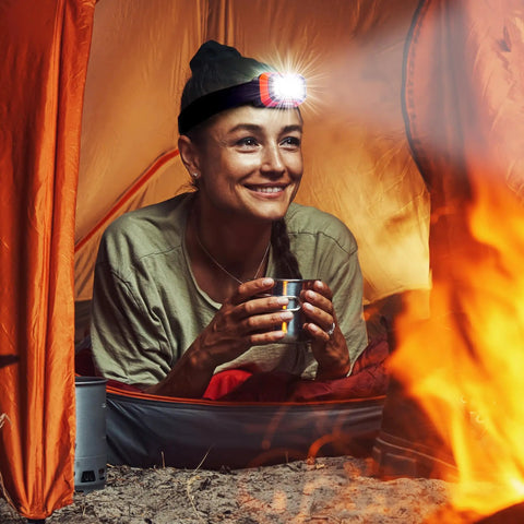 Camper wearing Rechargeable LED Headlamp With Wave Sensor Two Pack Ultra Bright 1000 Lumens in tent by fire, smiling.