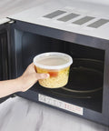 Person placing 16-Ounce To-Go Food Storage Containers With Lids, BPA Free, Leakproof Microwave Safe inside microwave