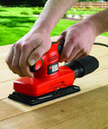 Badass Compact Electric Orbital Sander With Rugged Ergonomic Design And Turbo Spin Action in use on a wooden surface.