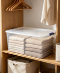 Ginormous 105 Quart Clear Storage Bin With Blue Secure Latch Heavy Duty Plastic Tote For Bulky Seasonal Gear And Bedding Keeps Your Space Spiffy And Makes Organization A Breeze, filled with neatly folded blankets on a wooden shelf.