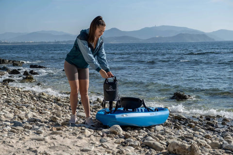 Person using Go-To Premium Waterproof Dry Bag Backpack For Kayaking And Outdoor Adventures, 5L black on rocky beach.
