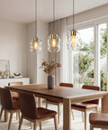 3 Pack Gold Pendant Lights For Kitchen Island Featuring 8.7 Inch Hand Blown Clear Art Glass Globes above wooden dining table.