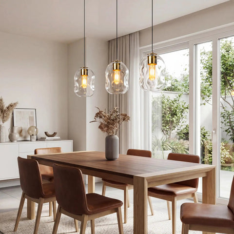 3 Pack Gold Pendant Lights For Kitchen Island Featuring 8.7 Inch Hand Blown Clear Art Glass Globes above wooden dining table.