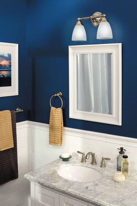 Brantford Style 2-Light Dual-Mount Vanity Light in Brushed Nickel with Frosted Glass above a bathroom mirror on blue wall