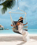 Person sitting on a Chill Indoor Outdoor Hammock Chair With Wooden Armrests, Steel Spreader Bar And Anti Slip Rings, on a beach