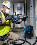 Bosch Bulldog SDS-Plus rotary hammer drill bit in use; blue bit attached to hammer on concrete with a worker in safety gear.