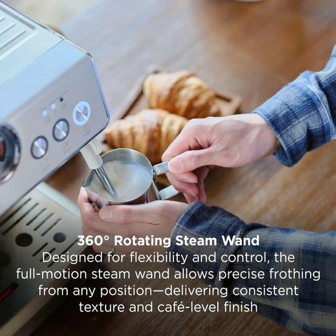 Person using Talos Semi Automatic Grind And Brew Espresso Machine With Built In Conical Burr Grinder 20 Bar Italian Pump Real Time Pressure Gauge Stainless Steel Lunar Finish For Barista Level Flavor At Home to froth milk with a steaming wand, with croissants in the background.
