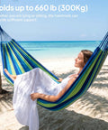 Woman relaxing on Ultra Comfy Cotton Hammock Portable Camping Hammock For Hanging With Tree Straps Sturdy Garden Fabric Hammock Up To 660 Lbs Includes Travel Bag Great For Camping Outdoor Indoor Patio Backyard Relaxation by the beach.