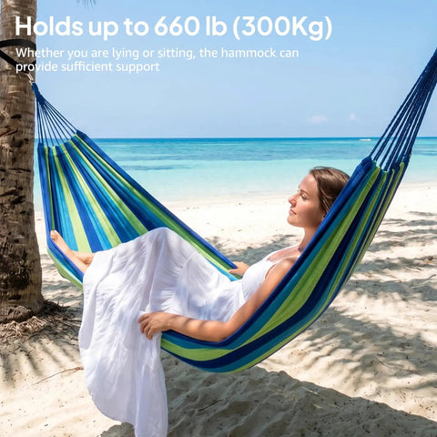 Woman relaxing on Ultra Comfy Cotton Hammock Portable Camping Hammock For Hanging With Tree Straps Sturdy Garden Fabric Hammock Up To 660 Lbs Includes Travel Bag Great For Camping Outdoor Indoor Patio Backyard Relaxation by the beach.