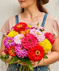 Woman holding a bouquet of bright zinnia flowers in various colors, showcasing blooms of Giant Flowered Zinnia Seeds Mix In Bright Colors.