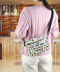 Just One More Geocache I Promise Crossbody Bag with colorful icons, worn by person in a cafe, showcasing adjustable strap and canvas design.