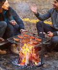 People grilling sausages on Portable Campfire Grill Grate For Fire Pit Foldable Stainless Steel With Height Adjustable Legs