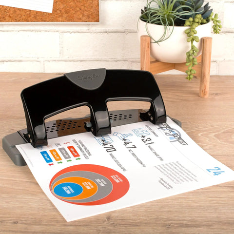 No Sweat Heavy Duty Three Hole Puncher With 20 Sheet Capacity Solid Steel Frame in use with printed paper on desk.