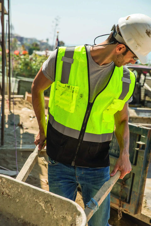 Boss Level Hi Vis Reflective Safety Vest Built Different To Keep You On Point All Shift Long With Durable Zipper Closure And Smart Black Bottom Mesh Panels For Road Work Projects, worn by a worker handling materials.