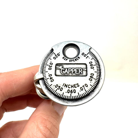 Hand holding Coin-Style Spark Plug Gap Tool For Quick Checks, 0.020-0.100 In Gap Range, Plated Steel Build, Pro Grade Gauge
